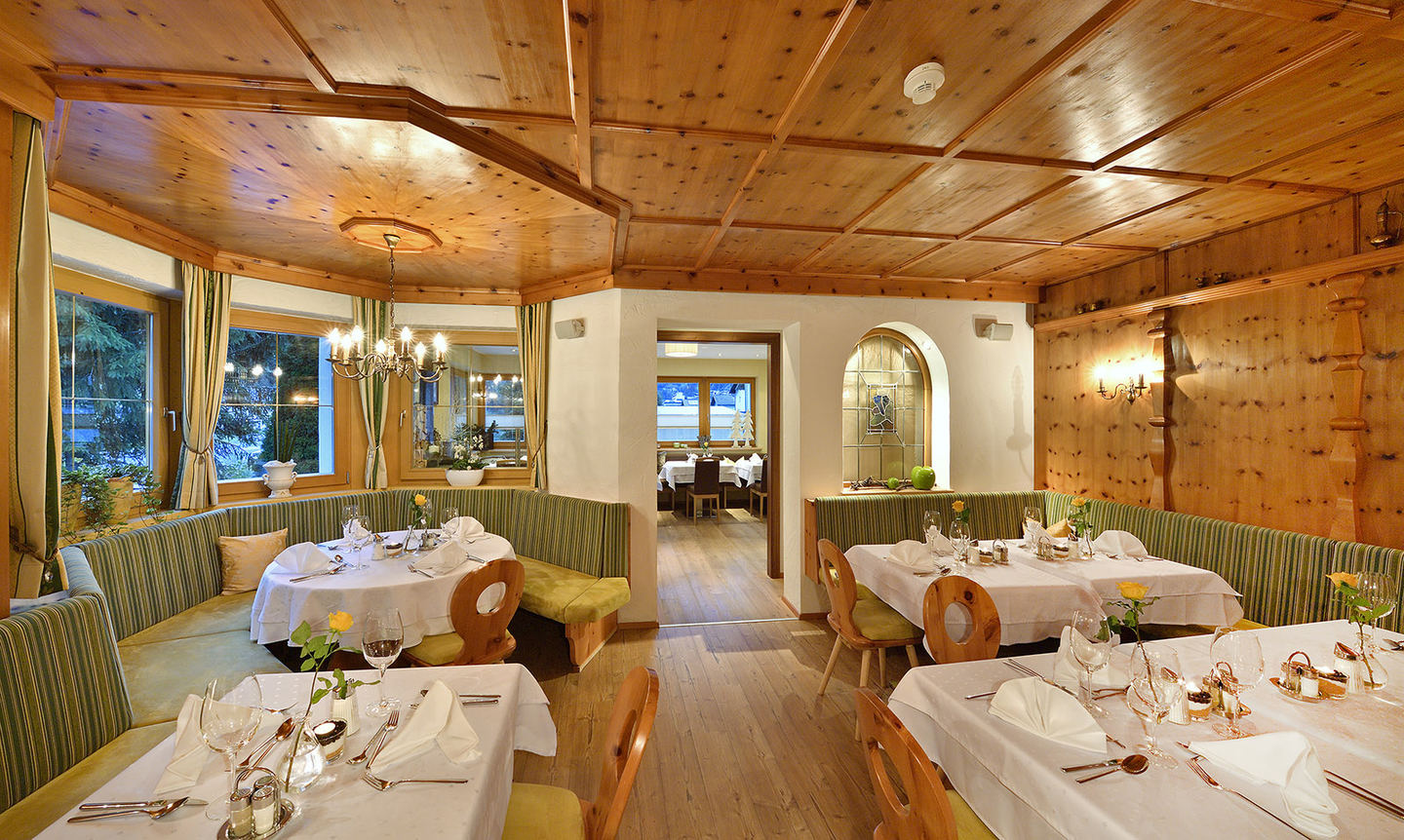 Dining room with wooden ceiling and laid tables at Hotel Enzian
